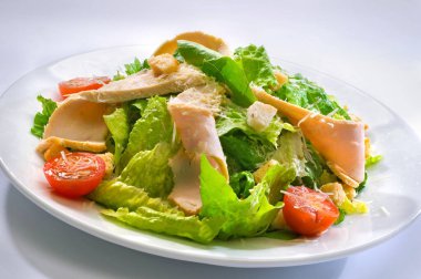 Camdan beyaz bir tabakta salata, vişneli domates, tavuk filetosu, kızarmış ekmek, marul ve rendelenmiş peynir.