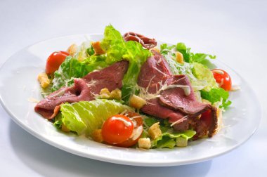 Camdan beyaz bir tabakta salata, vişneli domates, sığır eti, kızarmış ekmek, marul, rendelenmiş peynir ve sos.