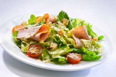 Çeri domates, jambon, kıtır ekmek, marul, rendelenmiş peynir ve soslu cam tabakta salata.