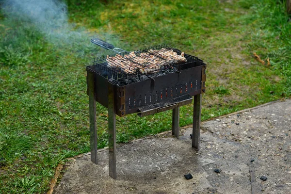 Burning firewood in the grill, smoke from the fire, a paper bag with charcoal for grilling, on a background of green grass