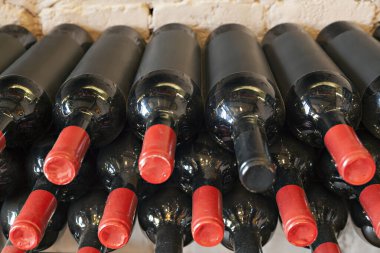 Yığılmış, kırmızı mantarlı siyah şarap şişeleri.