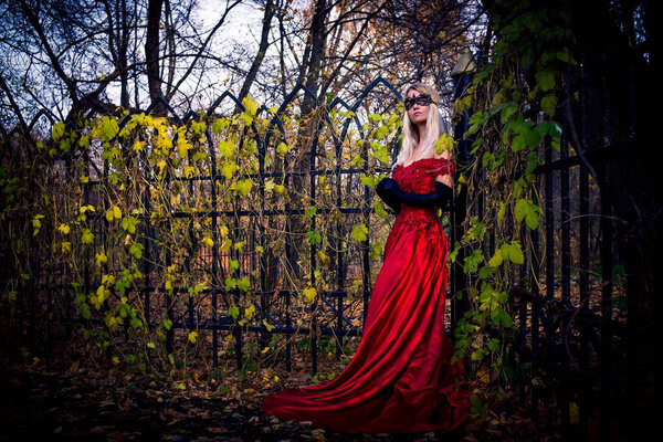 Mysterious woman in mask standing near fence. Autumn, fall