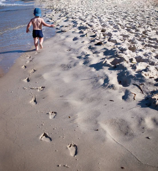 소년은 해변을 뛰어가서 발자국을 남긴다 — 스톡 사진