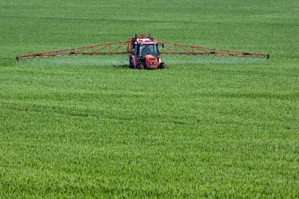 Trator pulverização de pesticidas em grande campo verde com grãos jovens — Fotografia de Stock