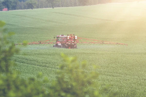 拖拉机在大绿色的原野上喷洒农药，与年轻的粮食 — 图库照片