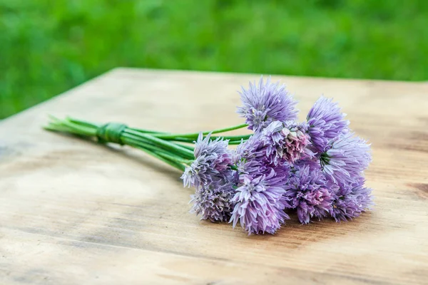 Ciboulette de fleurs attachée dans un snop sur une planche à découper en bois naturel — Photo