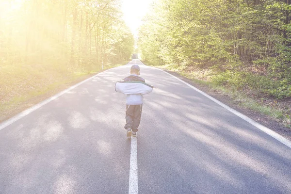 Menino andando por uma estrada no meio de uma floresta — Fotografia de Stock