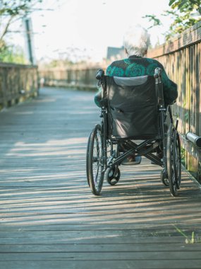 Tekerlekli sandalyede oturan yaşlı bir kadının güneş ışığına bakarken çekilmiş fotoğrafı..