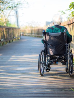 Tekerlekli sandalyede oturan yaşlı bir kadının güneş ışığına bakarken çekilmiş fotoğrafı..