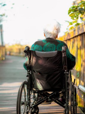 Tekerlekli sandalyede oturan yaşlı bir kadının güneş ışığına bakarken çekilmiş fotoğrafı..
