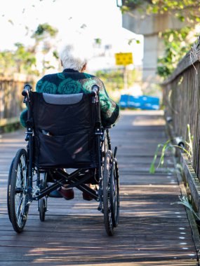 Tekerlekli sandalyede oturan yaşlı bir kadının güneş ışığına bakarken çekilmiş fotoğrafı..