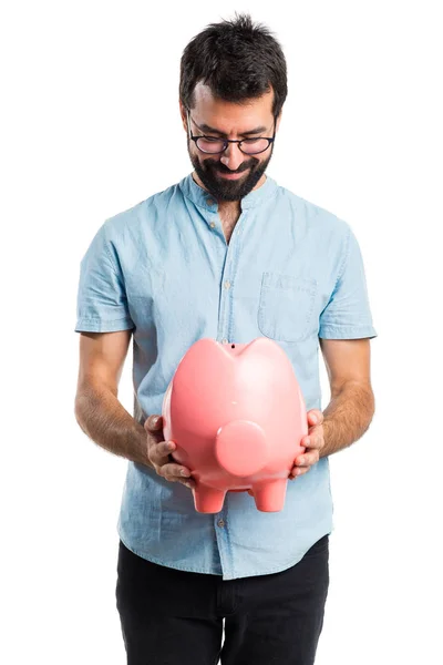Handsome man with blue glasses holding a piggybank — Stock Photo, Image