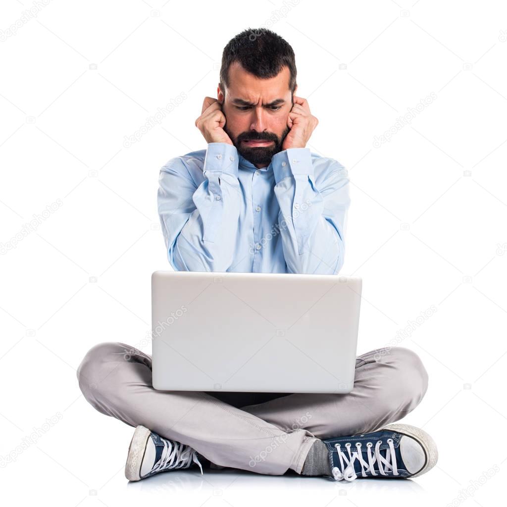 Man with laptop covering his ears