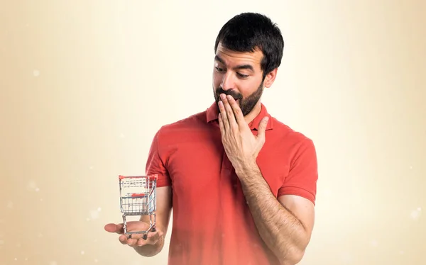 Handsome man holding a supermarket cart toy — Stock Photo, Image