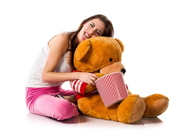 Chica feliz con pijama y sosteniendo un tazón de palomitas de maíz mientras juega con un animal de peluche —  Fotos de Stock