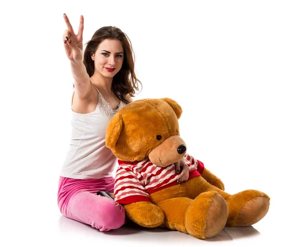 Chica con pijama haciendo gesto de victoria y jugando con peluche —  Fotos de Stock