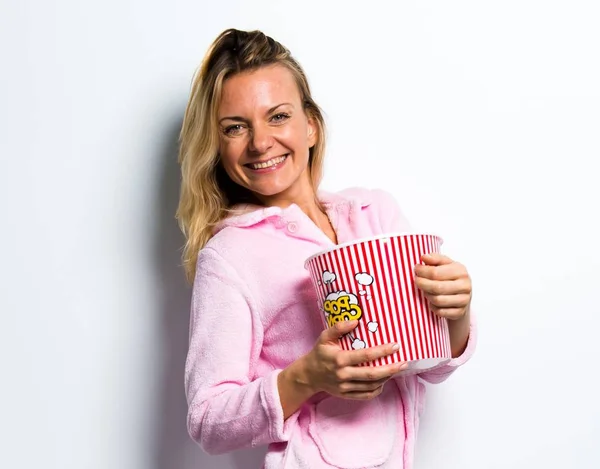 Hübsche blonde Frau im pinkfarbenen Morgenmantel, die Popcorn isst — Stockfoto