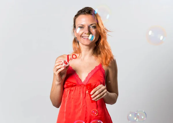 Mulher bonita com cabelo laranja soprando bolhas — Fotografia de Stock