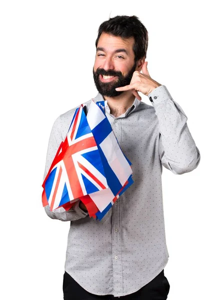 Красивий чоловік з бородою тримає багато прапорів і робить жест телефону — стокове фото