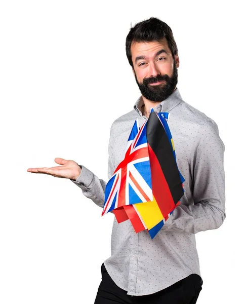 Homem bonito com barba segurando muitas bandeiras e segurando algo — Fotografia de Stock
