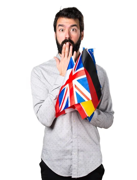 Knappe man met baard houden vele vlaggen en verrassing gebaar maken — Stockfoto