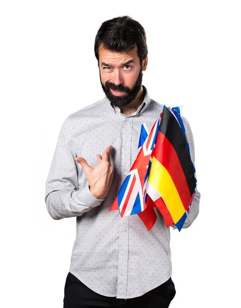 Homem bonito com barba segurando muitas bandeiras e fazendo gesto surpresa — Fotografia de Stock