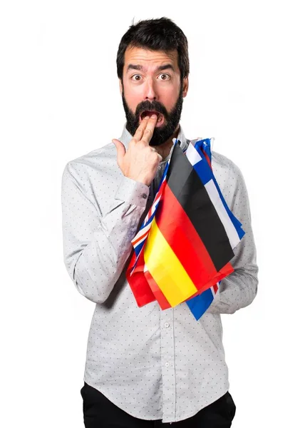 Handsome man with beard holding many flags and making vomiting gesture — Stock Photo, Image