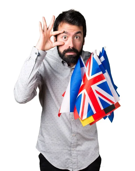 Hombre guapo con barba sosteniendo muchas banderas y mostrando algo —  Fotos de Stock