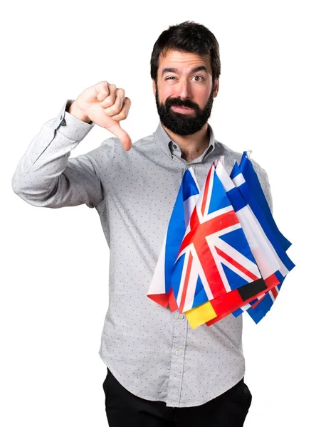 Birçok bayrak tutan ve kötü sinyal yapma sakallı yakışıklı adam — Stok fotoğraf