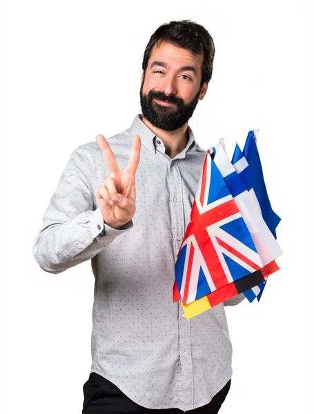 Homem bonito com barba segurando muitas bandeiras e fazendo gesto de vitória — Fotografia de Stock