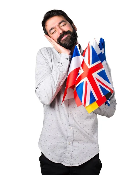 Homem bonito com barba segurando muitas bandeiras e fazendo gestos de sono — Fotografia de Stock