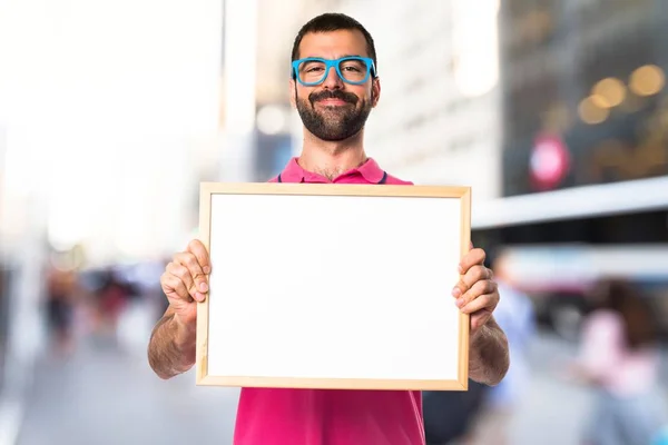 Homem com roupas coloridas segurando um cartaz vazio — Fotografia de Stock