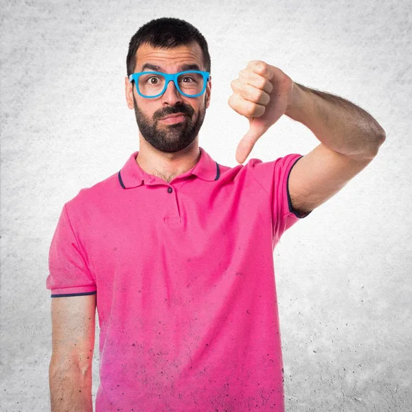 Homme avec des vêtements colorés faisant mauvais signal sur le dos texturé gris — Photo