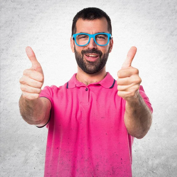 Homem em roupas coloridas com o polegar para cima em backgroun texturizado cinza — Fotografia de Stock
