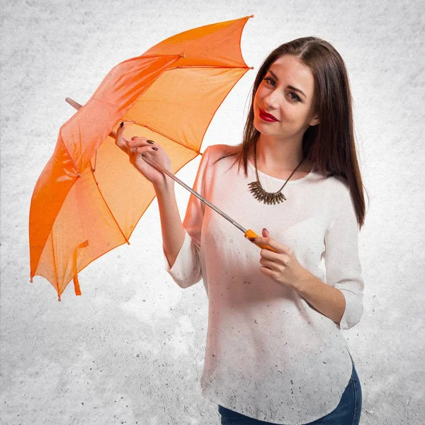 Ganska ung flicka som innehar ett paraply på texturerat grå bak — Stockfoto