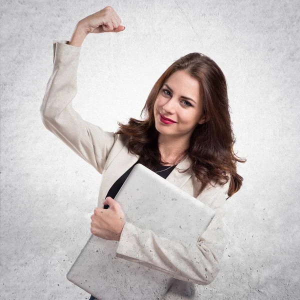 Lucky pretty young business woman with laptop on textured grey b — Stock Photo, Image