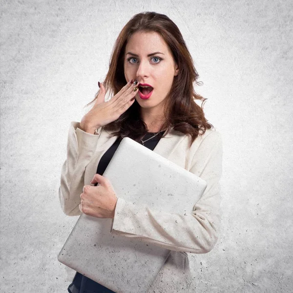 Surprised pretty young business woman with laptop on textured gr — Stock Photo, Image