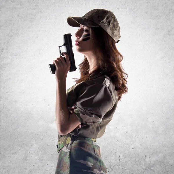 Militära flicka håller en pistol på texturerat grå bakgrund — Stockfoto