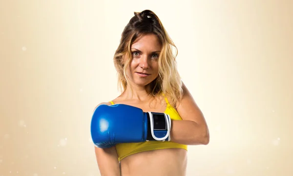 Pretty blonde woman with blue boxing gloves on ocher background