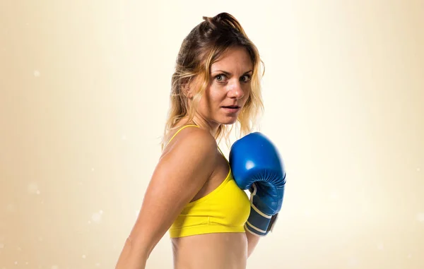 Mulher loira bonita com luvas de boxe azul no fundo ocre — Fotografia de Stock