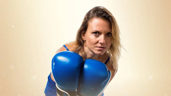 Pretty blonde woman with blue boxing gloves on ocher background