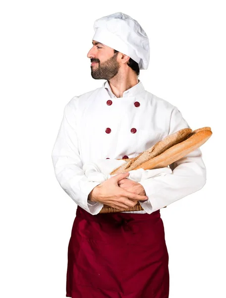 Młody piekarz trzyma chleb i patrząc boczne — Zdjęcie stockowe