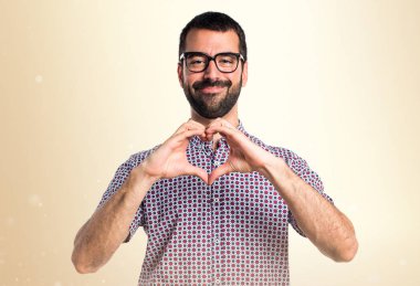 Koyu sarı backgrou elleri ile bir kalp yapma gözlüklü adam