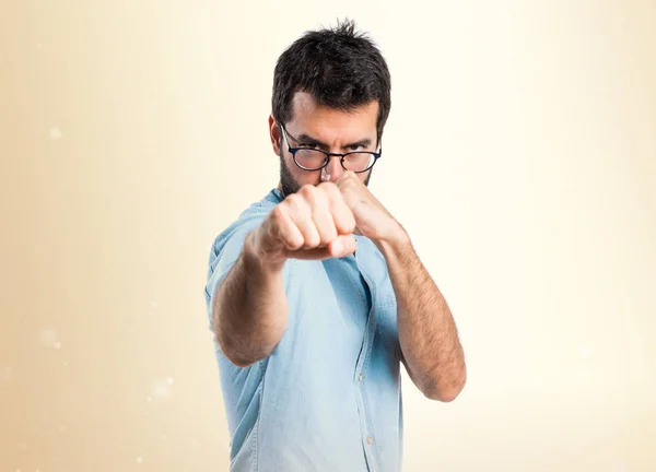 Schöner Mann mit blauer Brille gibt einen Punch auf ockerfarbenem Hintergrund — Stockfoto