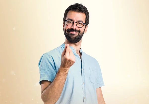 Hombre guapo con gafas azules haciendo gesto de dinero en ocre bac —  Fotos de Stock