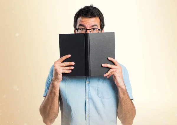 Hombre guapo con gafas azules libro de lectura sobre fondo ocre —  Fotos de Stock
