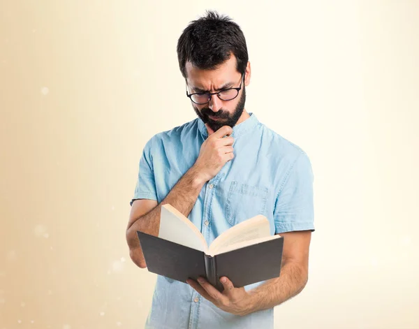 Hombre guapo con gafas azules libro de lectura sobre fondo ocre —  Fotos de Stock