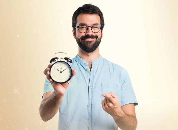 Bel homme avec des lunettes bleues tenant horloge sur fond ocre — Photo