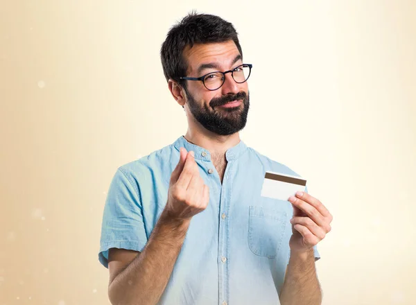 Knappe man met blauwe glazen een credit card bedrijf op okergeel ba — Stockfoto