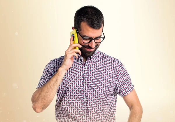 Człowiek w okularach, mówienie do telefonów na tle ochry — Zdjęcie stockowe